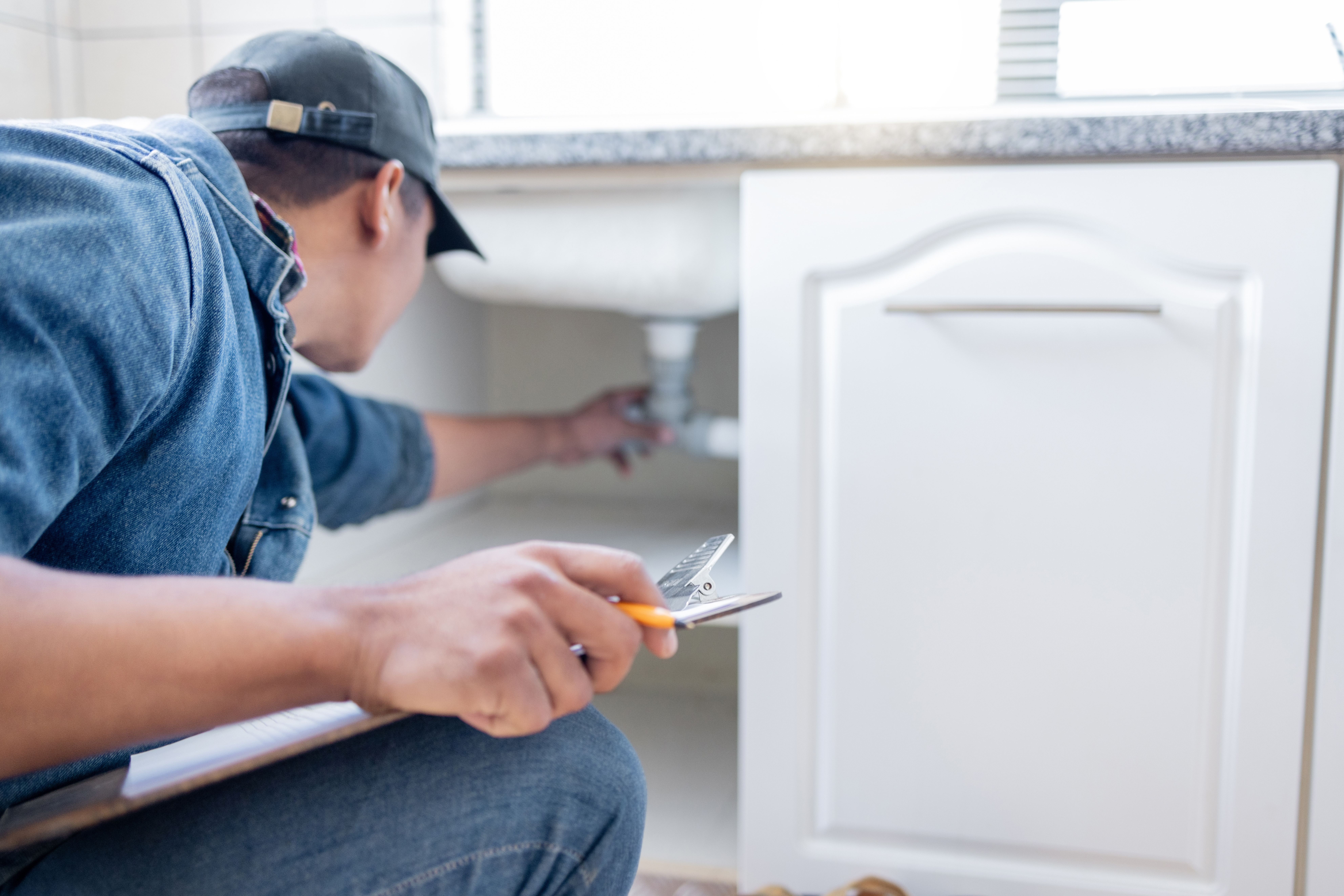 Plumber checking out the piping under the sink to determine what services need to be done as a solution to the problem