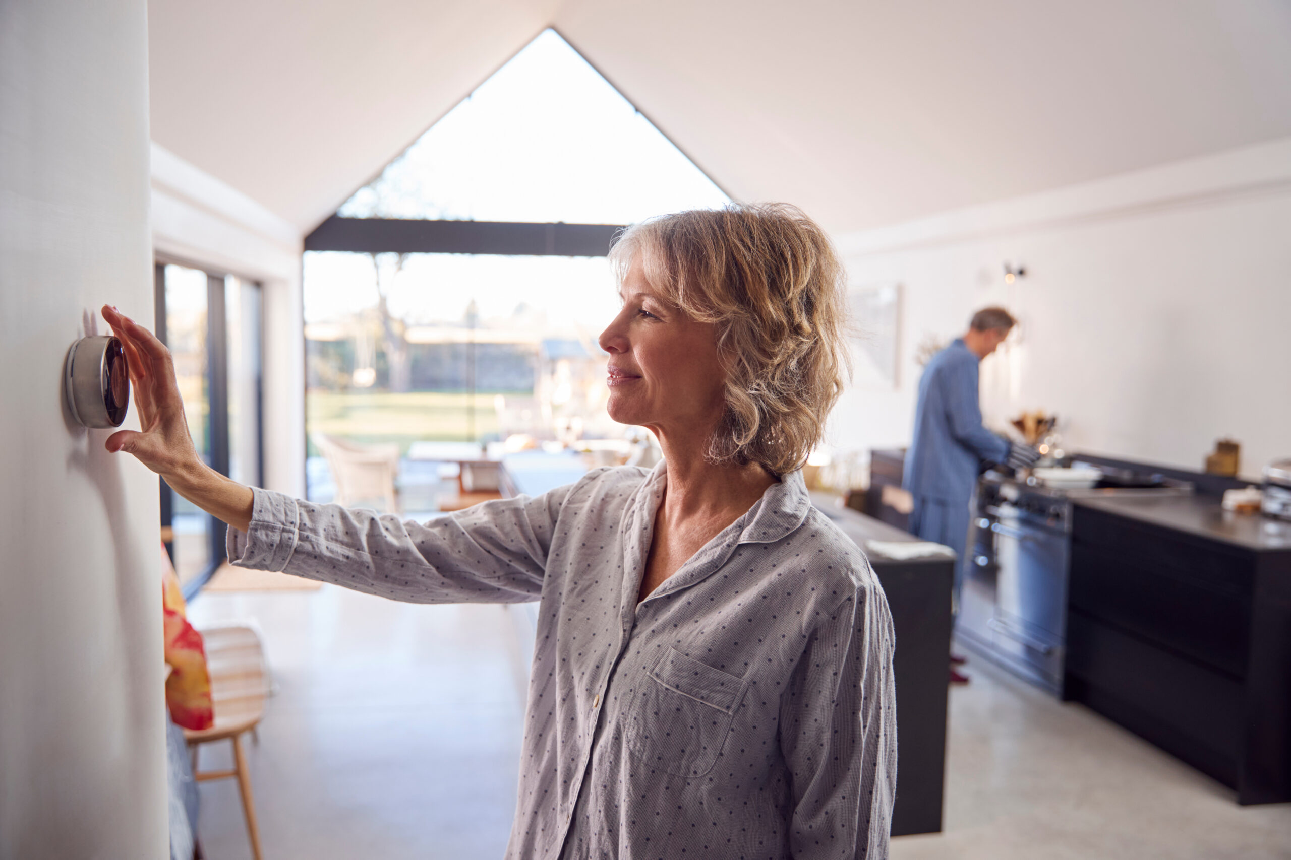 Mature Woman Adjusting Wall Mounted Digital Central Heating Thermostat Control At Home